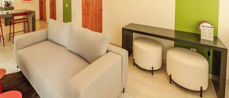 Una sala de estar moderna con un sofá gris, un pequeño comedor con una silla roja y una pared verde de acento.