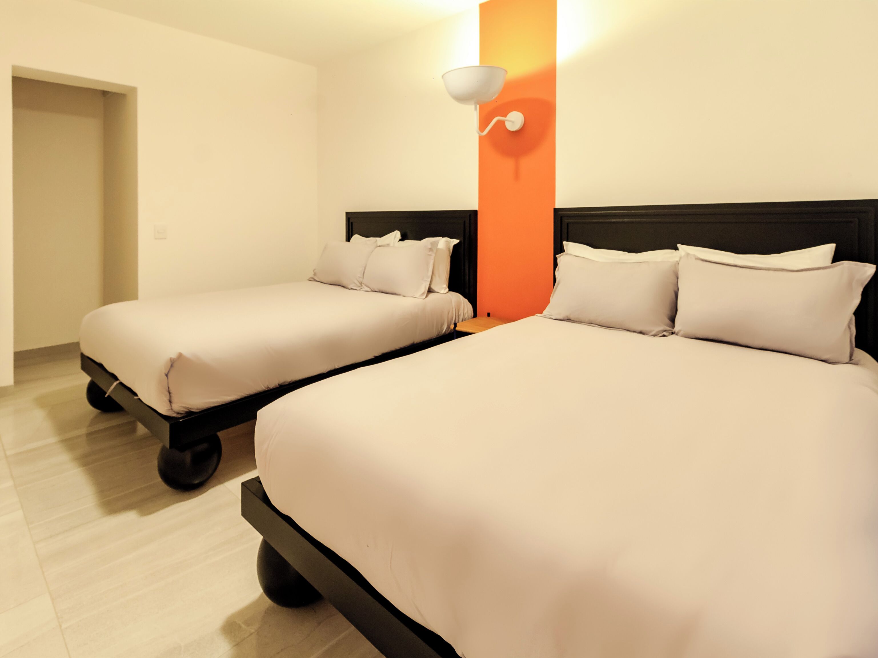 Hotellihuone, jossa on kaksi erillistä sänkyä, yöpöytä ja seinään kiinnitetty valaisin.