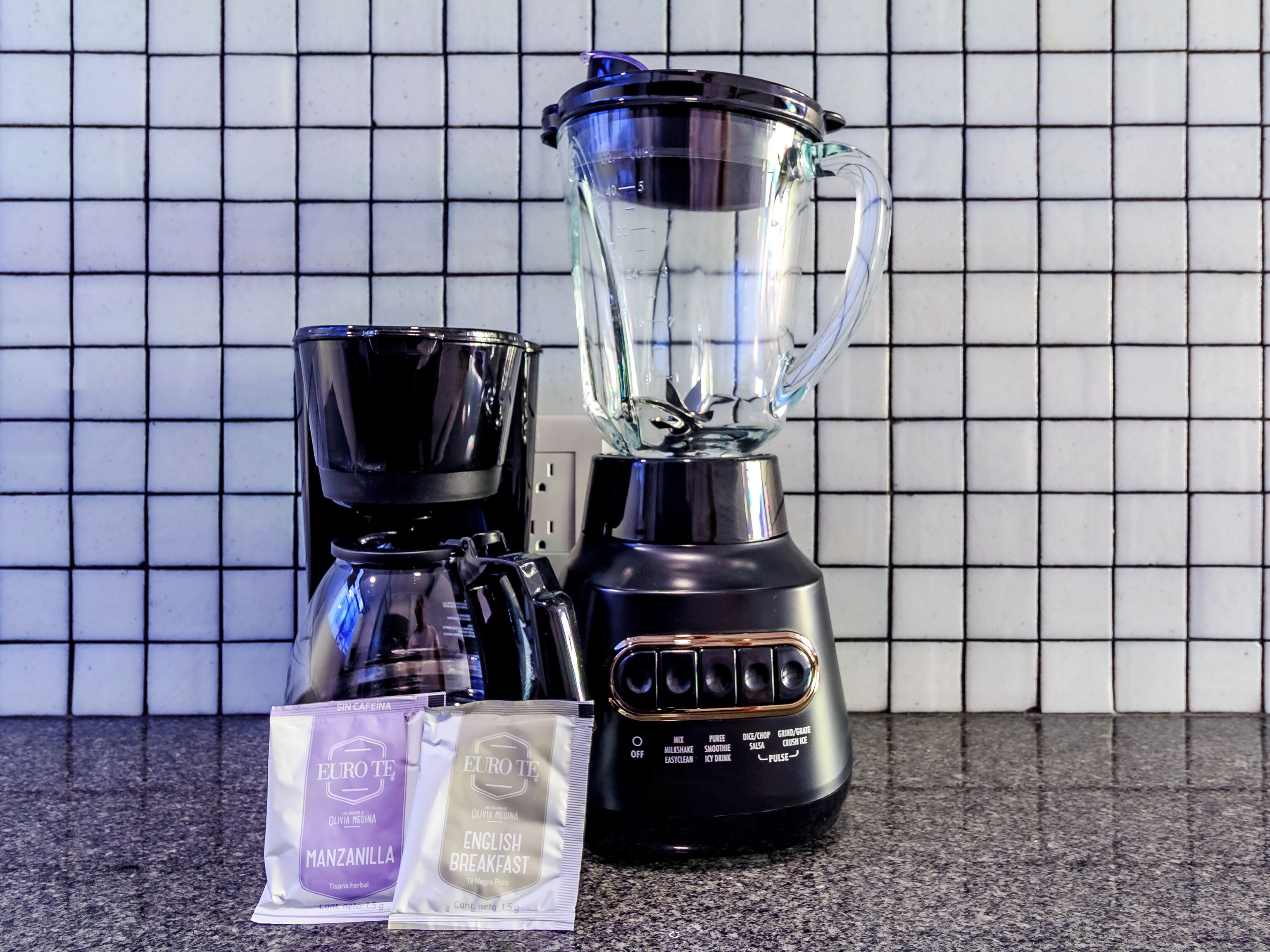 Una cocina con una licuadora, una cafetera y dos sobres de café.