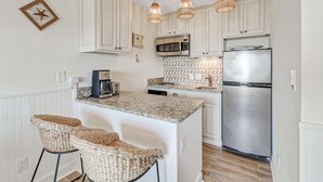 A kitchen with white cabinets, a stainless steel refrigerator, a microwave, a coffee maker, and three woven stools. - Oceanfront Villa with Pool (Hilton Head Island)