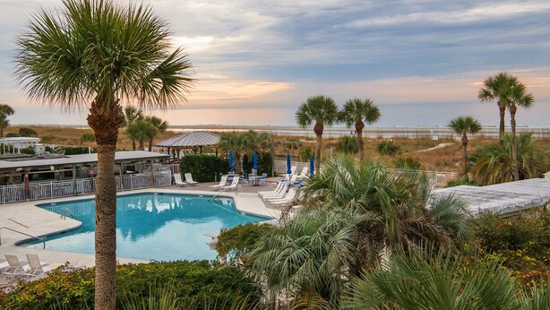 A pool area with lounge chairs and umbrellas, surrounded by palm trees and a view of the beach. - Oceanfront Villa with Pool (Hilton Head Island)