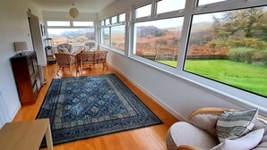 A room with a large window, a blue patterned rug, wicker chairs, and a view of the outdoors. - Erisgeir Sleeps 6 With Private Grounds (Isle of Mull)