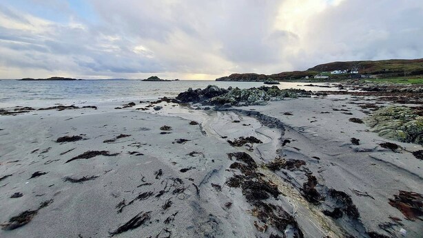 A beach with rocky outcrops and a distant view of houses on a hilly landscape. - Erisgeir Sleeps 6 With Private Grounds (Isle of Mull)