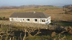 A white house with a stone wall in front, set in a rural landscape with hills and a clear sky. - Erisgeir Sleeps 6 With Private Grounds (Isle of Mull)
