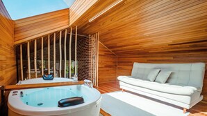 Une cabane en bois avec un jacuzzi, un canapé et une vue sur l’extérieur.