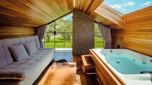 Une pièce chaleureuse avec un plafond en bois, un canapé, un jacuzzi et une vue sur un paysage verdoyant.