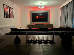 A living room with a TV mounted on the wall displaying 'NETFLIX', a sofa, a coffee table with candles, and a radiator. - Modern Apartment Free Parking Wifi Edgbaston (Birmingham)