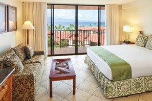 Ein Hotelzimmer mit Bett, einer Couch, einem Tisch und einem Balkon mit Blick auf das Meer und Gebäude.