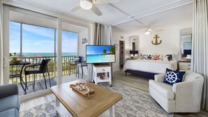 Une chambre dotée d’un balcon, d’un lit, d’une télévision et d’un coin repas avec une table et des chaises.