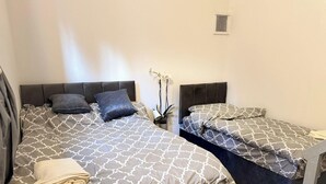 A double bed with patterned bedding, a bedside table with a plant, and a small window. - Entire Studio With 2 Extra Beds (Purley)