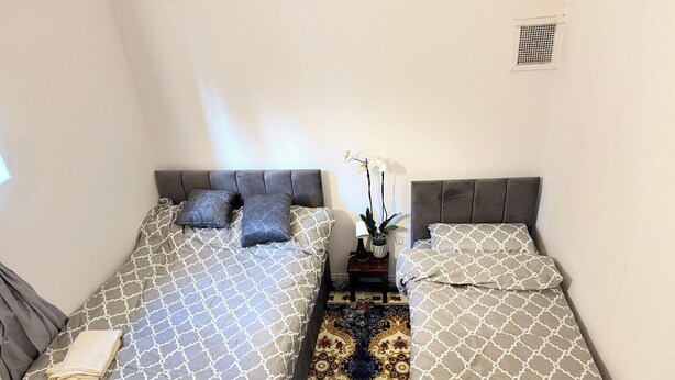 Ein Zimmer mit zwei Betten, jeweils mit gemusterten Bettwäsche und Kissen, einem kleinen Tisch mit Lampe und Pflanze sowie einem dekorativen Teppich.