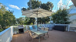 A wooden deck with a table and chairs, a grill, and a large umbrella.