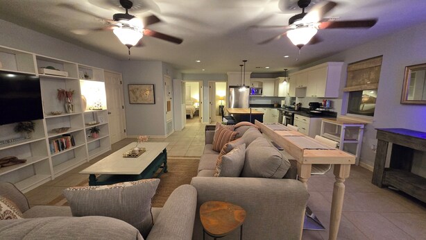 A modern living room with a sofa, coffee table, and TV. There is a kitchen in the background with a dining area.