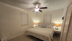 A bedroom with a bed, two bedside tables with lamps, a ceiling fan, and a door.