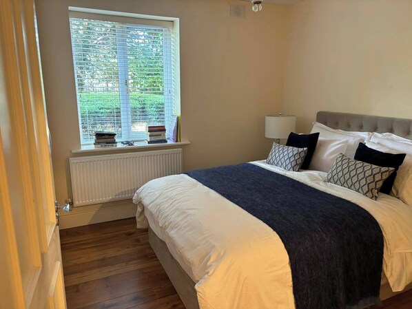 A bedroom with a bed, a window with blinds, a radiator, and a lamp.