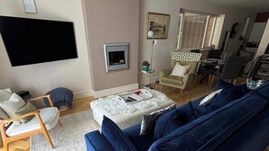 Una sala de estar con un sofá azul, televisor, chimenea y comedor.