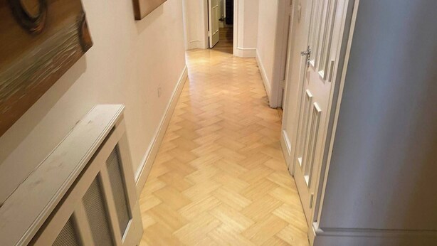 Un pasillo con piso de parqué tipo espiga, un radiador blanco y un armario gris.