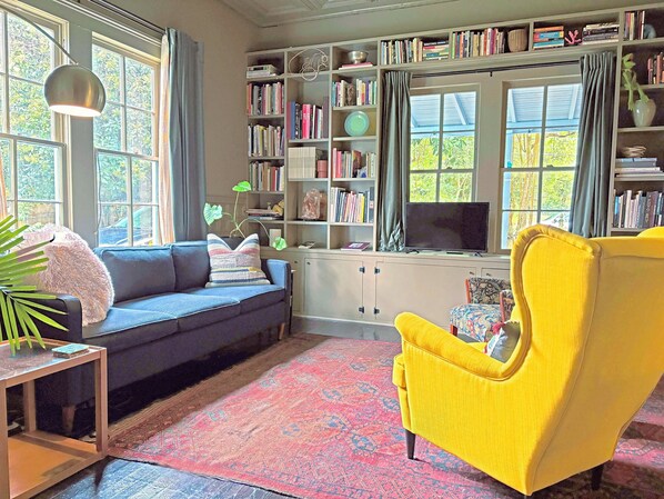 Un salon avec un canapé, un fauteuil jaune, une bibliothèque et un téléviseur.