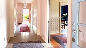 A hallway with a wooden floor, a red rug, and a door leading to a room with a dark wall and a plant. - Charming Home 2 miles to UGA (Athens)
