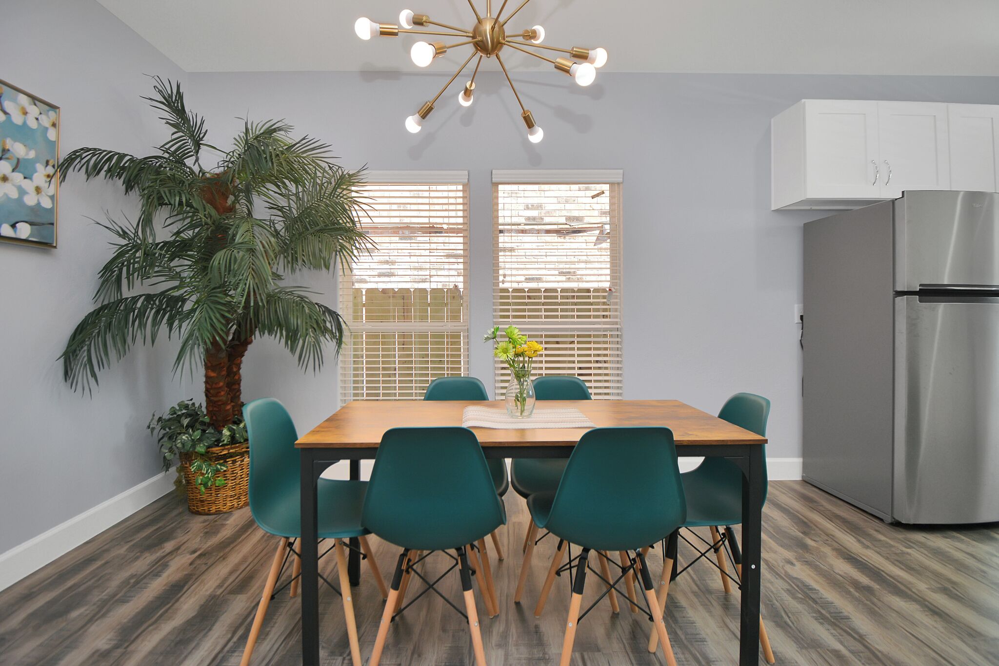 A modern kitchen with a dining table, chairs, a refrigerator, and a large potted plant.