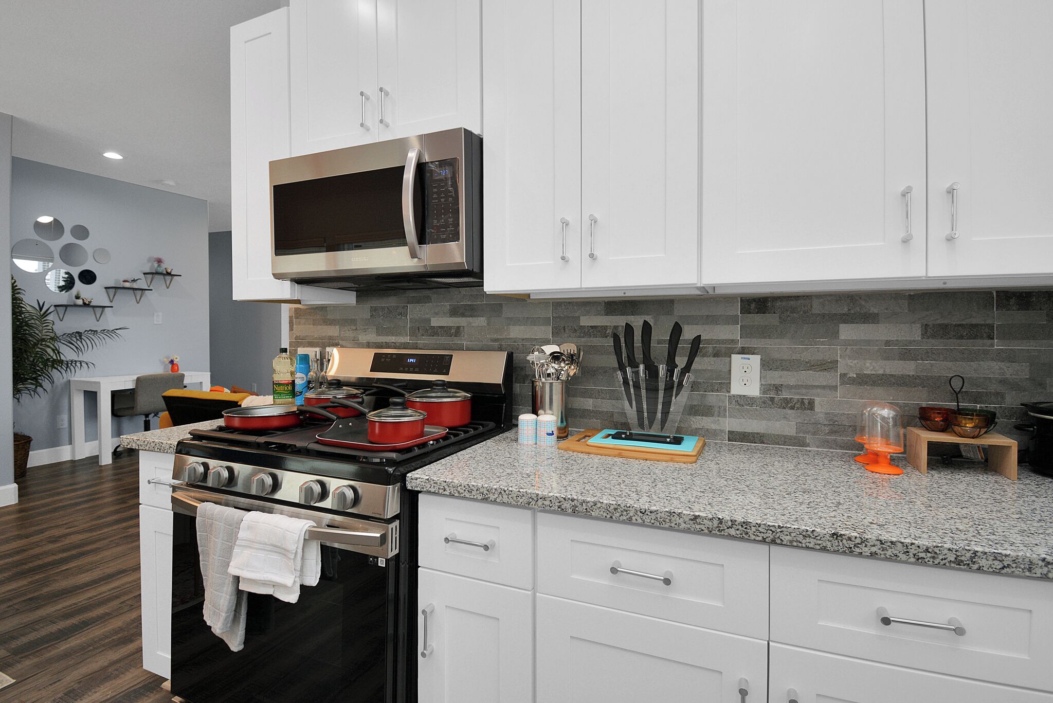 A modern kitchen with white cabinets, a stainless steel microwave, a gas stove, and granite countertops.