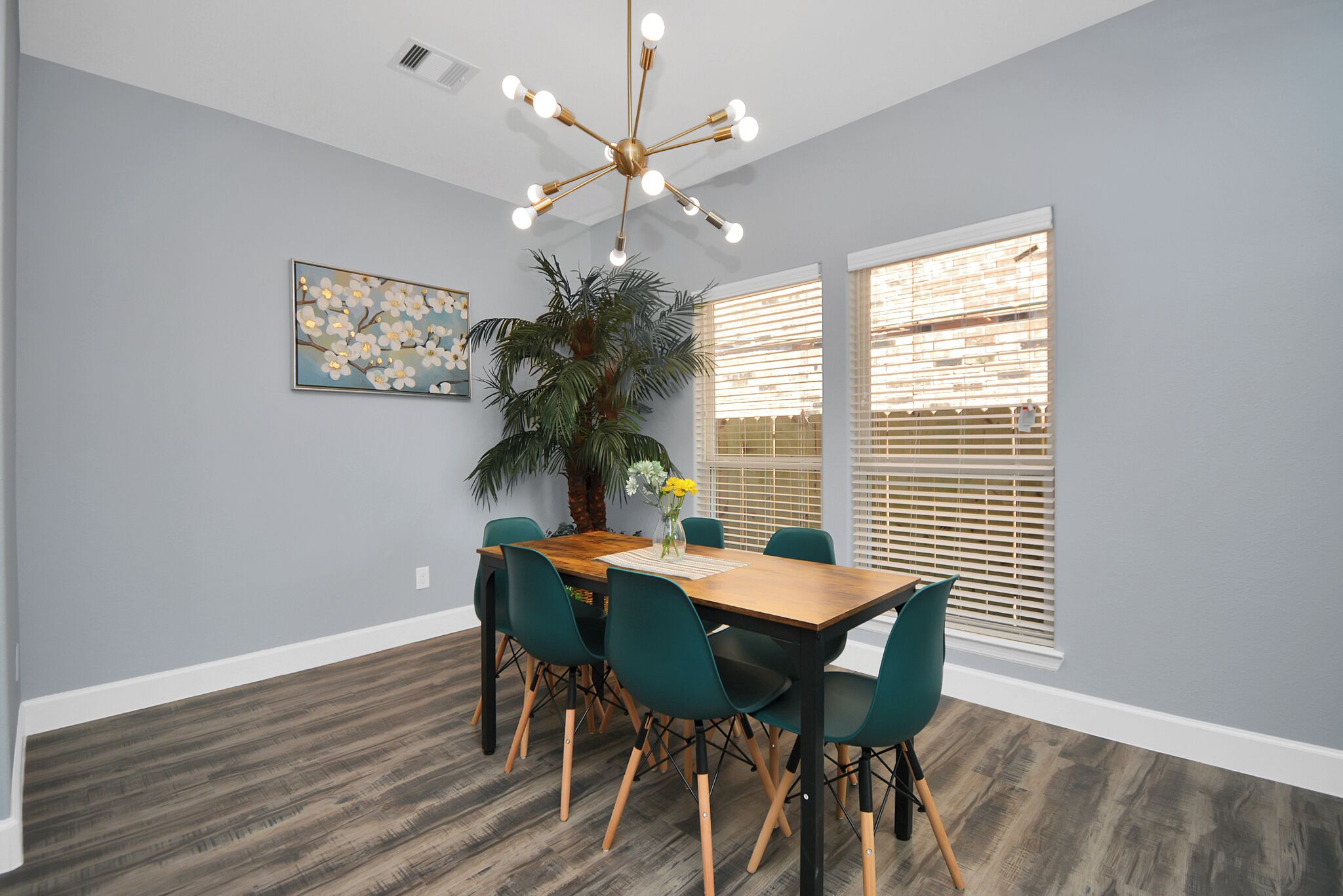 A dining area with a wooden table, green chairs, a large plant, and a ceiling light fixture.