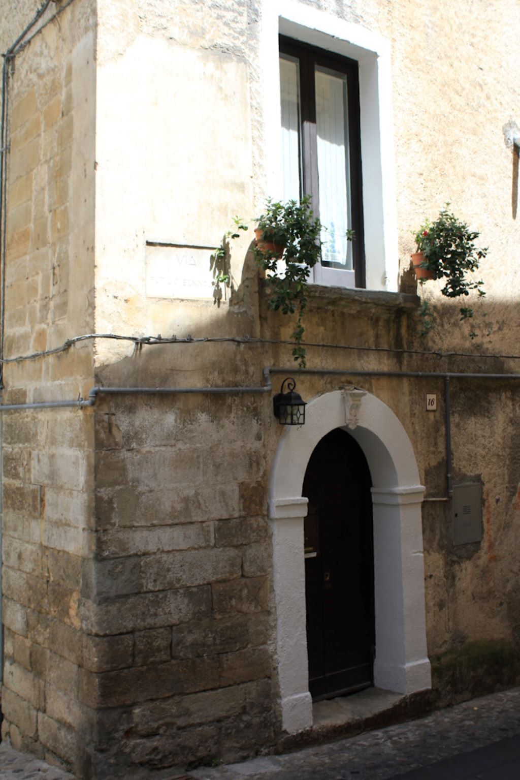 Ein Steinhaus mit einer schwarzen Tür und einem weißen Bogen. Ein Fenster mit weißem Rahmen und ein Blumentopf auf dem Sims.
