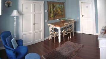 A room with a dining table, chairs, a blue armchair, a white cabinet, and a patterned rug.