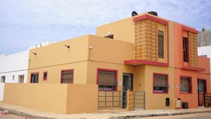 A two-story building with a beige facade, red-framed windows, and a brick accent wall. - Furnished MinVilla (duplex)  (Ouad-Eddahab Dakhla)