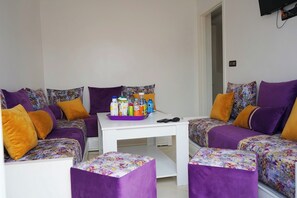 A cozy room with two purple sofas, a white table with a tray of beverages, and matching purple ottomans.