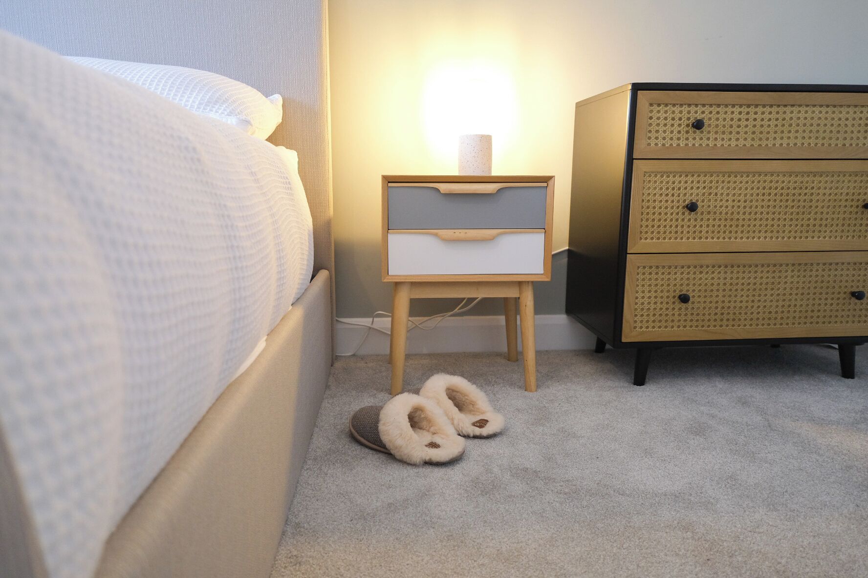 Ein Schlafzimmer mit einem Bett, einem Nachttisch mit Lampe, einem kleinen Holzbeistelltisch und einer Körbeschranke.