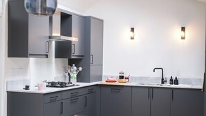Una cocina moderna con armarios oscuros, una estufa a gas y un lavamanos. Hay dos luces empotradas en la pared y una cafetera sobre la encimera.