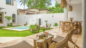 En moderne udendørs terrasse med swimmingpool, fletmøbler og et spiseområde.
