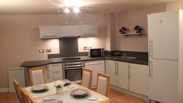 A compact kitchen with a dining table set for four, a microwave, oven, dishwasher, and a refrigerator.