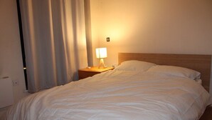 A neatly made bed with a wooden headboard, a bedside lamp, and a curtain partially drawn to the side.