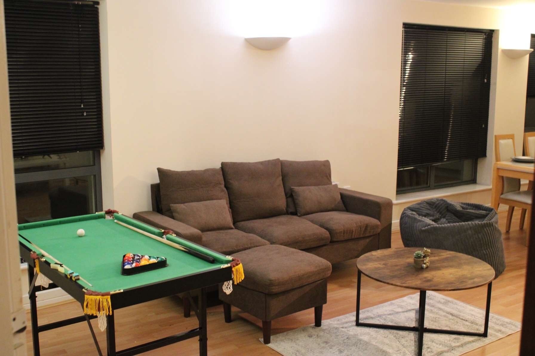 A living room with a pool table, a sofa, a round coffee table, and a bean bag chair.