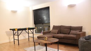 A living room with a brown sofa, a small round coffee table, a pool table, and a bean bag.