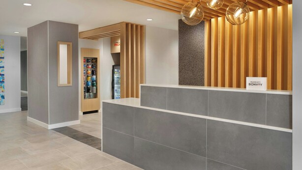 A reception area with a wooden reception desk, a wall-mounted sign, and a shelf with bottled water. - Towneplace Suites By Marriott Crown Point (Crown Point)