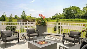 An outdoor patio with wicker furniture, a fire pit, and a view of a green landscape. - Towneplace Suites By Marriott Crown Point (Crown Point)