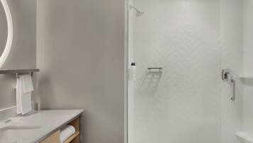 Une salle de bain moderne avec une douche carrelée de motifs en chevrons blancs, un lavabo blanc avec un miroir et une étagère en bois où sont posées des serviettes.