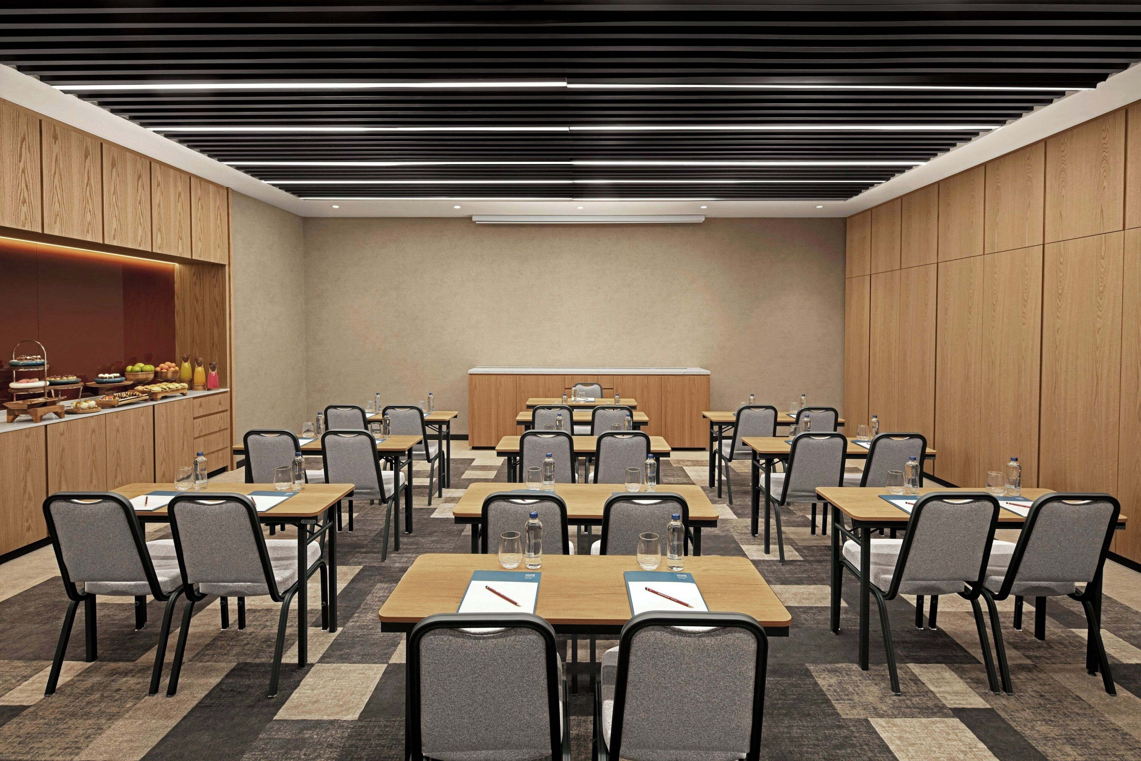 Un salón de conferencias con varias mesas y sillas, equipado con botellas de agua y blocs de notas.