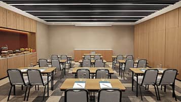Un salón de conferencias con varias mesas y sillas, equipado con botellas de agua y blocs de notas.