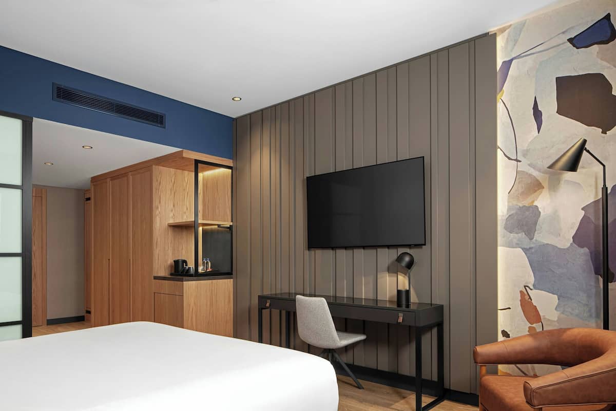 Une chambre d’hôtel comprenant un lit, un bureau avec une chaise, un téléviseur et un mur au décor texturé.