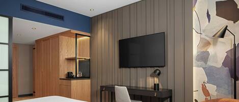 A hotel room with a bed, a desk with a chair, a TV, and a wall with a textured design.