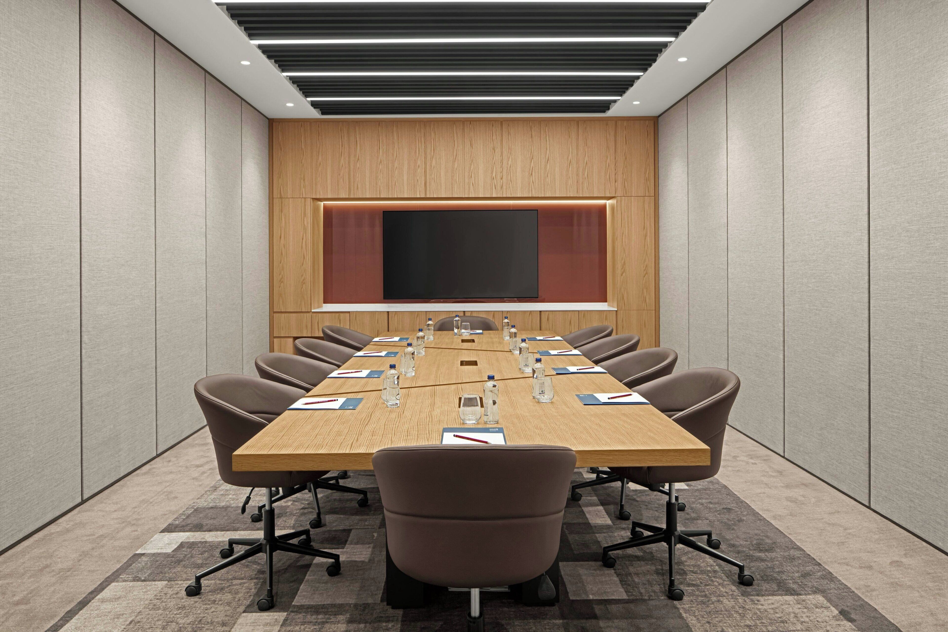 A conference room with a long table, chairs, and a large screen.