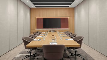 A conference room with a long table, chairs, and a large screen.