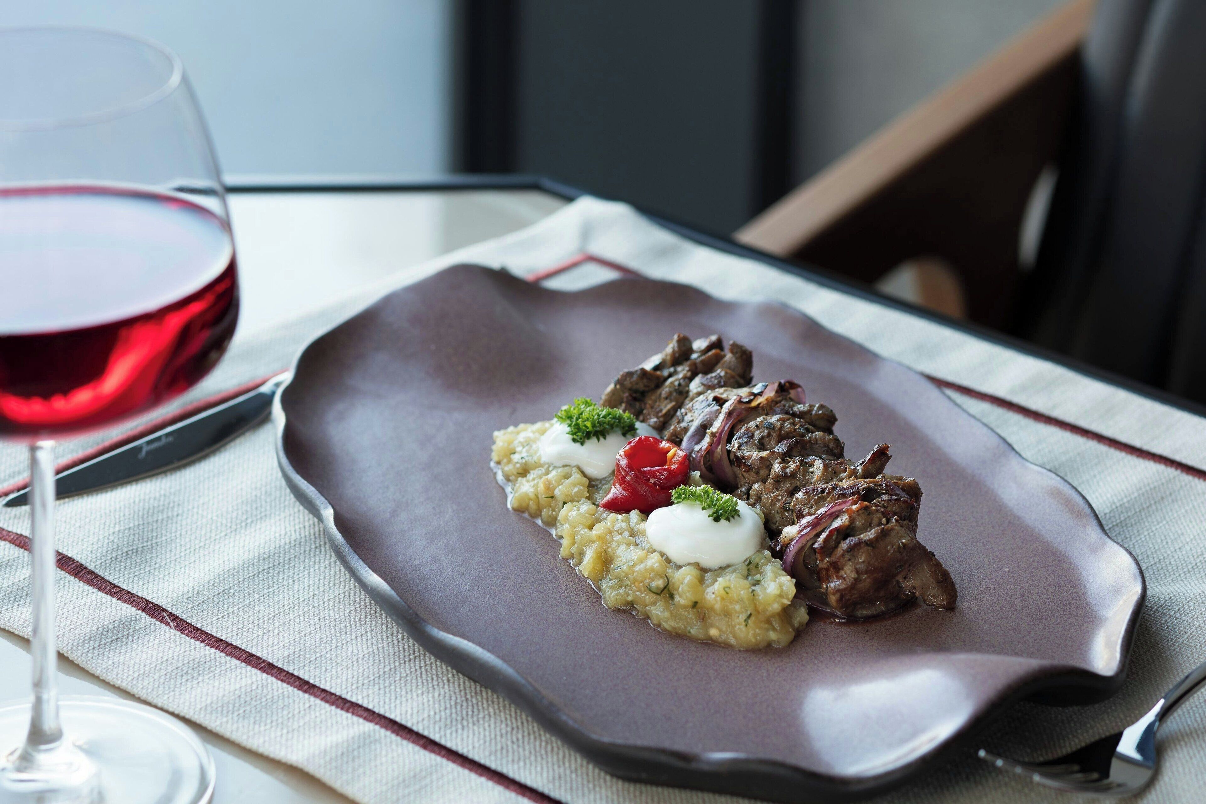 A plate of food with a glass of red wine on a table.