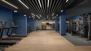 Une salle de sport équipée de tapis de course, d’appareils de musculation et dotée d’un plancher en bois.