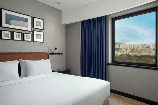A hotel room with a bed, a nightstand, a lamp, a city view, and framed artwork on the wall. - Four Points By Sheraton Istanbul Pendik (Istanbul)