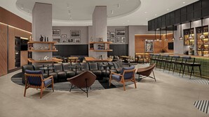 Un espace lounge moderne avec un aménagement central autour d’un coin salon, un bar doté d’un comptoir vert et un mur décoré de tableaux encadrés.